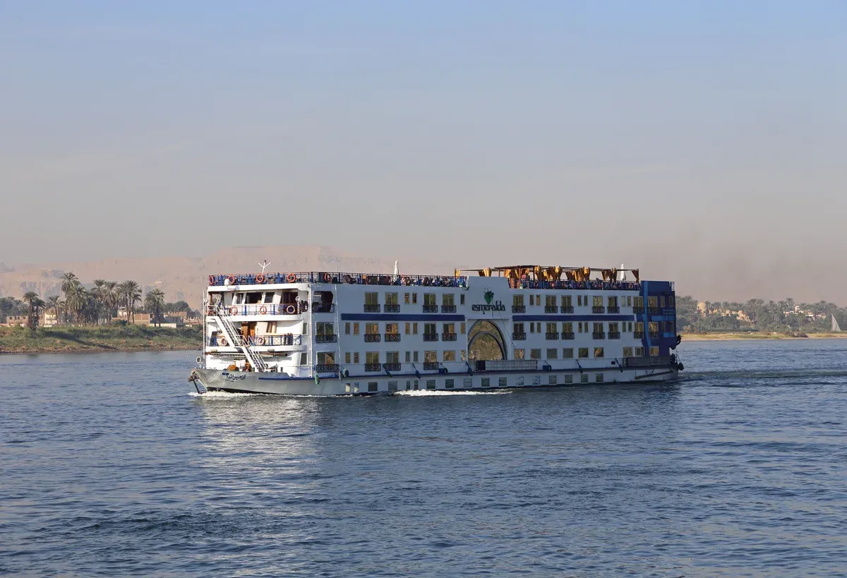 A four-deck cruise ship sailing past the Luxor West Bank on a Nile river cruise